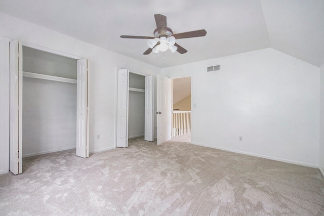 unfurnished bedroom with lofted ceiling, ceiling fan, light colored carpet, and two closets