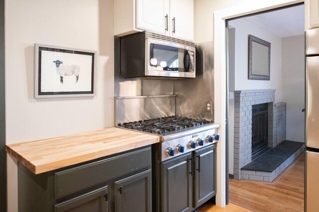 kitchen featuring wooden counters, a brick fireplace, stainless steel appliances, white cabinets, and light hardwood / wood-style floors