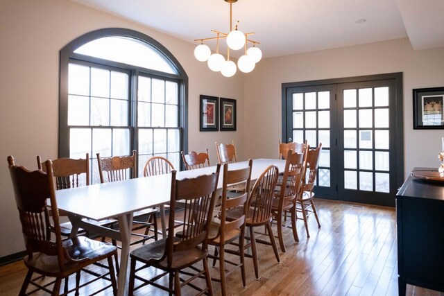 dining area featuring french doors, light wood-type flooring, and an inviting chandelier