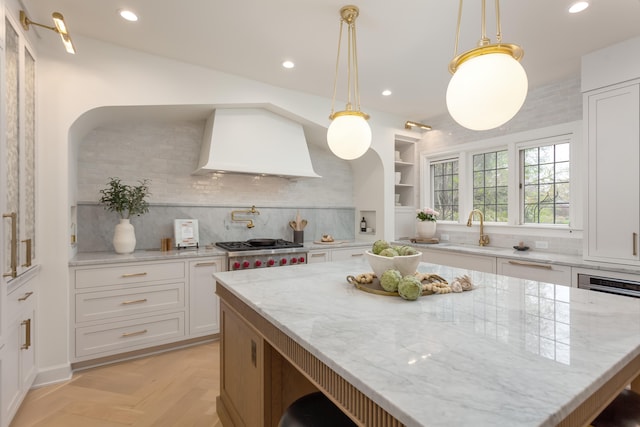 kitchen with light stone countertops, light parquet flooring, hanging light fixtures, and custom exhaust hood