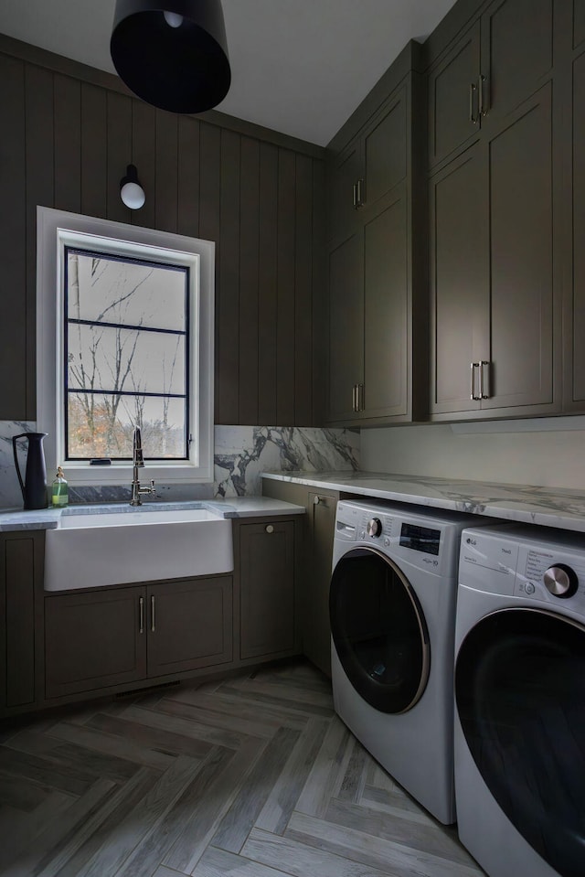 washroom with washing machine and clothes dryer, sink, cabinets, light parquet floors, and wooden walls