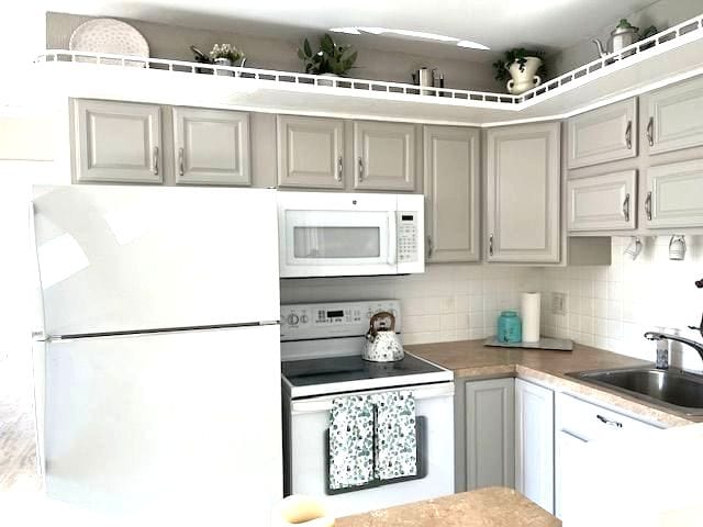 kitchen featuring tasteful backsplash, gray cabinetry, sink, and white appliances