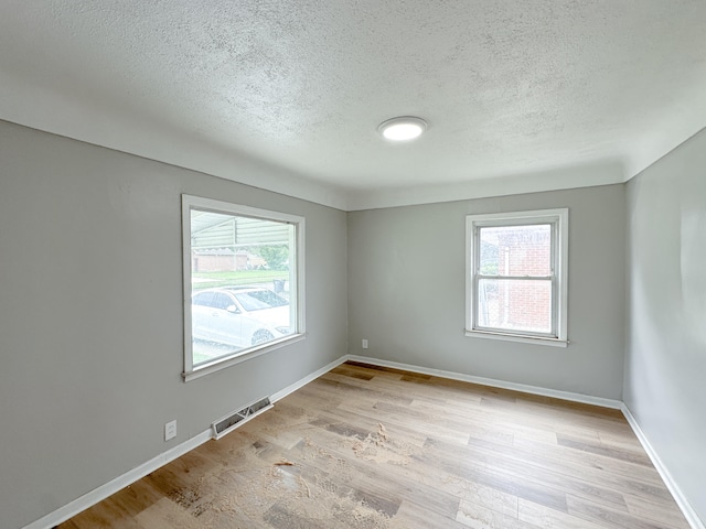 empty room with a healthy amount of sunlight, light wood-type flooring, and a textured ceiling