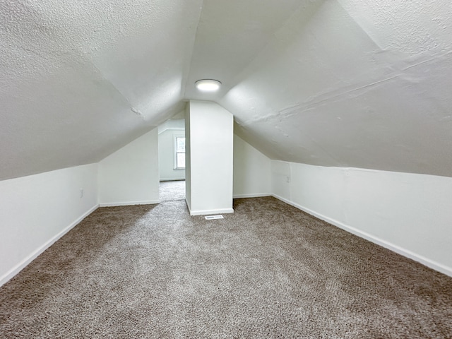 additional living space featuring a textured ceiling, carpet, and vaulted ceiling