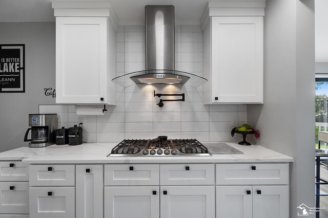 kitchen with white cabinetry, light stone countertops, stainless steel gas cooktop, and wall chimney range hood