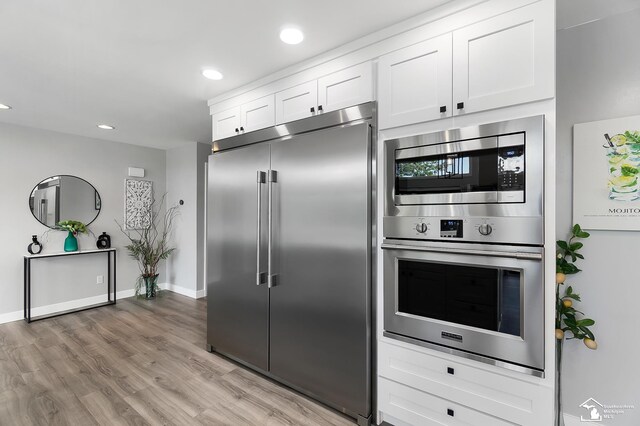 kitchen with built in appliances, white cabinetry, and light hardwood / wood-style flooring