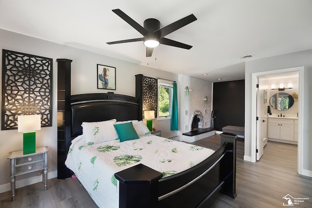 bedroom featuring hardwood / wood-style flooring, ensuite bath, ceiling fan, and a brick fireplace