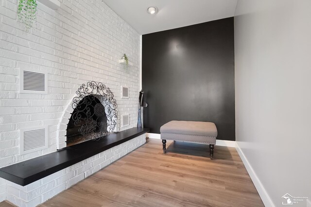 sitting room with a brick fireplace, wood-type flooring, and brick wall