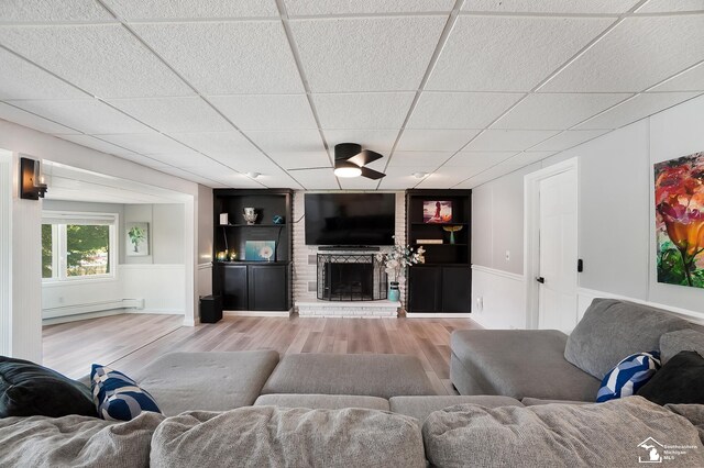 living room with a baseboard heating unit, a fireplace, wood-type flooring, and a paneled ceiling