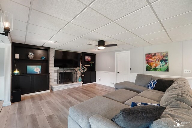 living room featuring a paneled ceiling, built in features, ceiling fan, hardwood / wood-style floors, and a brick fireplace