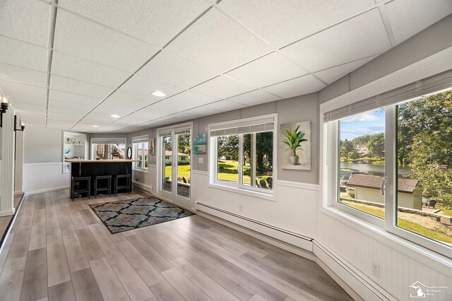 interior space with a baseboard radiator, a water view, plenty of natural light, and a paneled ceiling