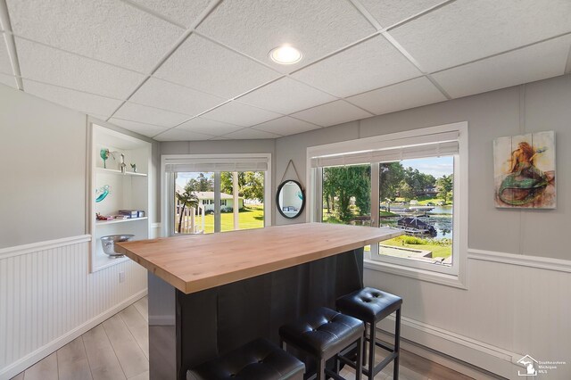 interior space featuring wood counters, a drop ceiling, a breakfast bar area, and light wood-type flooring