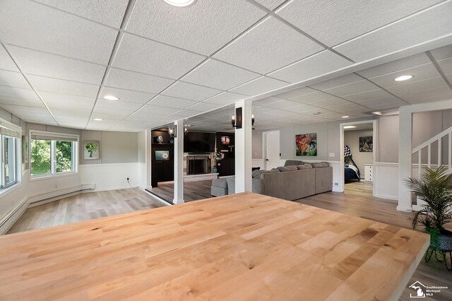 unfurnished dining area featuring a drop ceiling, a brick fireplace, and wood-type flooring