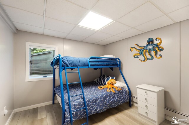 bedroom with a paneled ceiling, light hardwood / wood-style floors, and baseboard heating