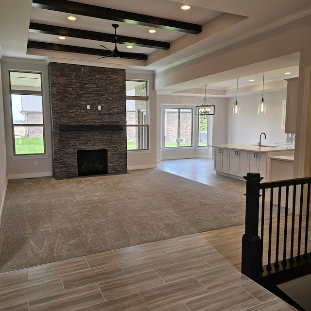 unfurnished living room with light carpet, a stone fireplace, a raised ceiling, ceiling fan with notable chandelier, and sink