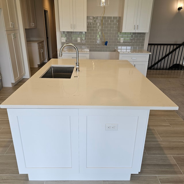 kitchen with light stone countertops, white cabinetry, decorative backsplash, sink, and a center island with sink