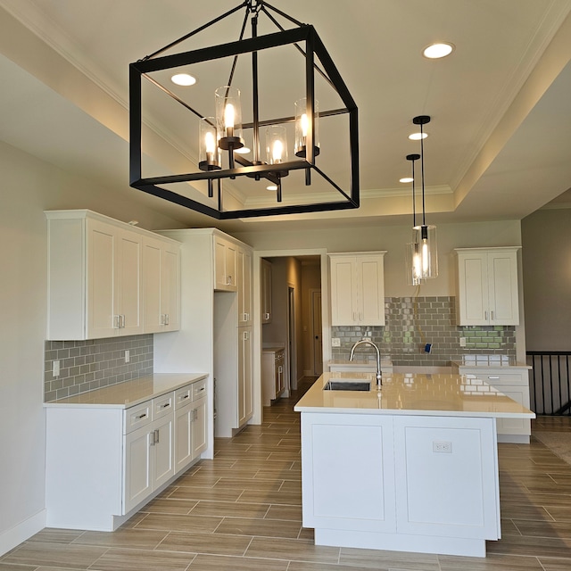 kitchen with white cabinetry, sink, hanging light fixtures, a raised ceiling, and a center island with sink