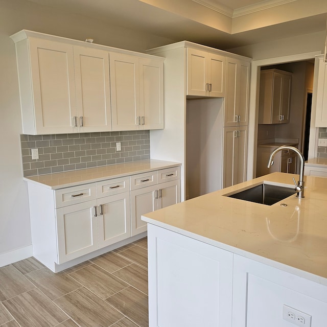 kitchen featuring tasteful backsplash, sink, crown molding, white cabinetry, and light stone countertops