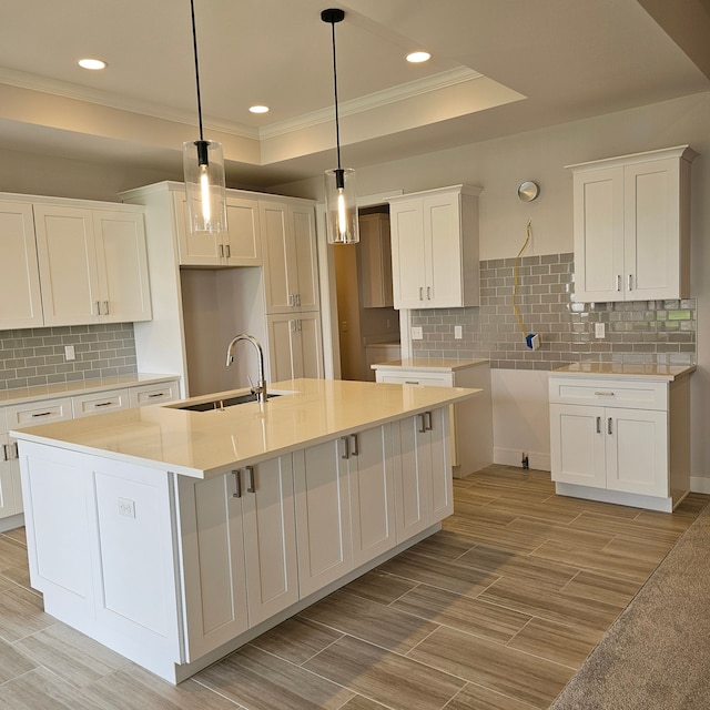 kitchen with a center island with sink, a raised ceiling, pendant lighting, white cabinets, and sink