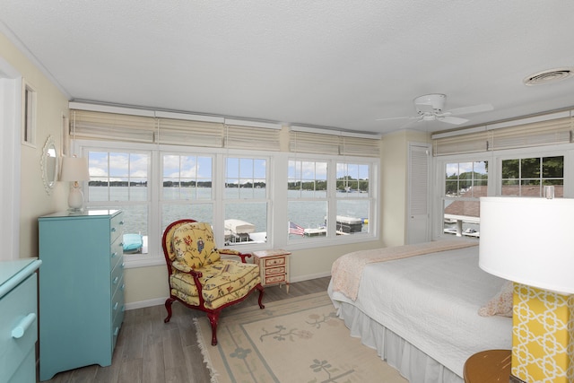 bedroom with ceiling fan, a water view, wood-type flooring, and a textured ceiling