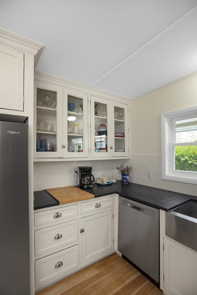 kitchen with appliances with stainless steel finishes, light hardwood / wood-style flooring, white cabinetry, and tasteful backsplash