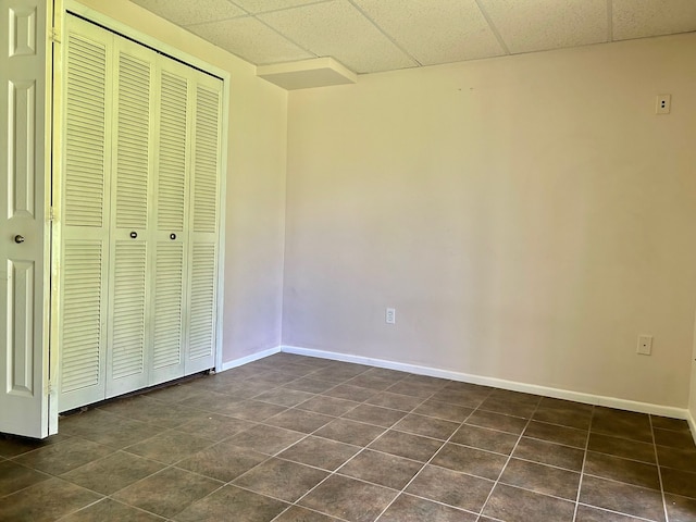 unfurnished bedroom with a paneled ceiling, dark tile patterned flooring, and a closet