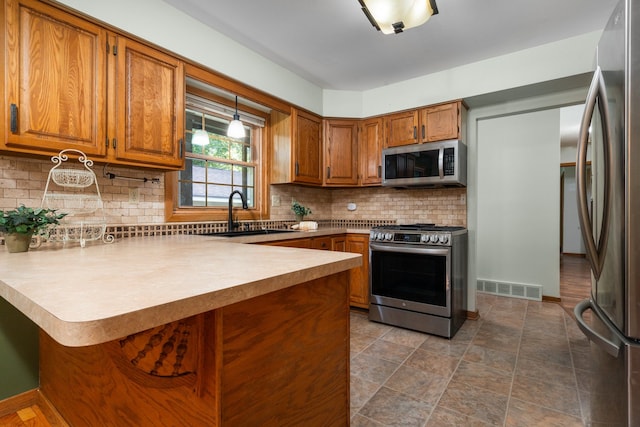 kitchen featuring sink, tasteful backsplash, kitchen peninsula, pendant lighting, and appliances with stainless steel finishes