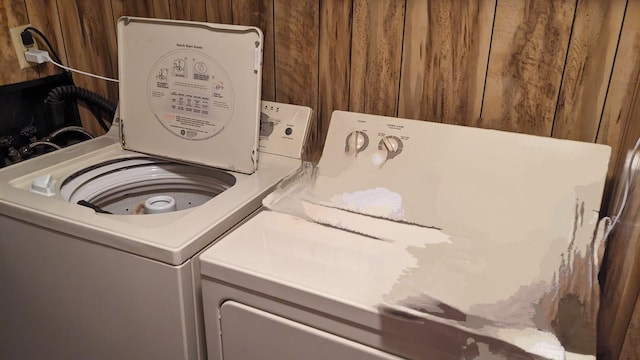 clothes washing area with washer and dryer and wood walls