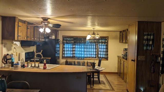 kitchen featuring ceiling fan with notable chandelier, black fridge, sink, light hardwood / wood-style floors, and kitchen peninsula