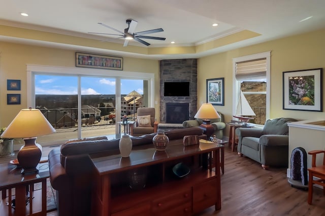 living room featuring ceiling fan, a raised ceiling, crown molding, wood-type flooring, and a fireplace