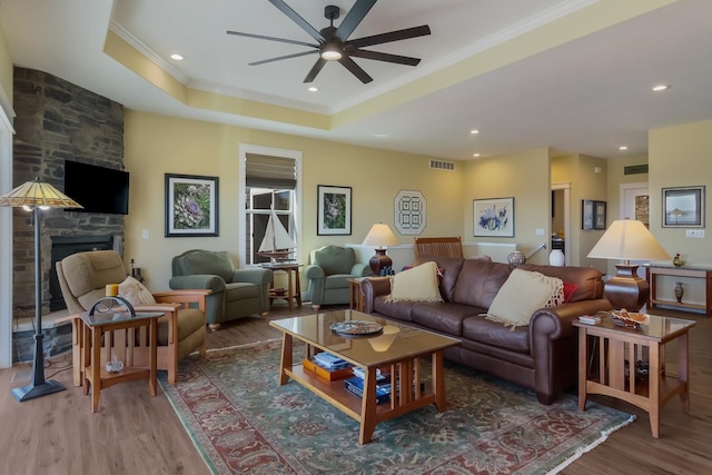 living room featuring a fireplace, a tray ceiling, hardwood / wood-style flooring, and ceiling fan