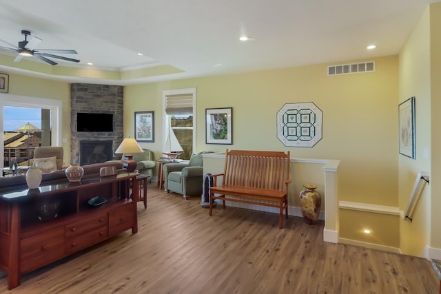 living room with wood-type flooring, a stone fireplace, and ceiling fan