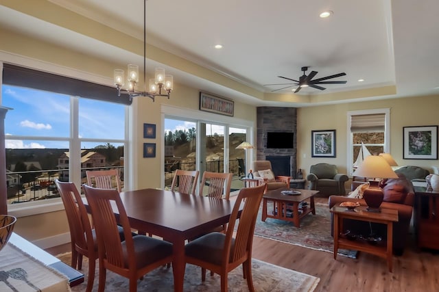 dining space featuring ceiling fan with notable chandelier, light hardwood / wood-style floors, a raised ceiling, and a fireplace