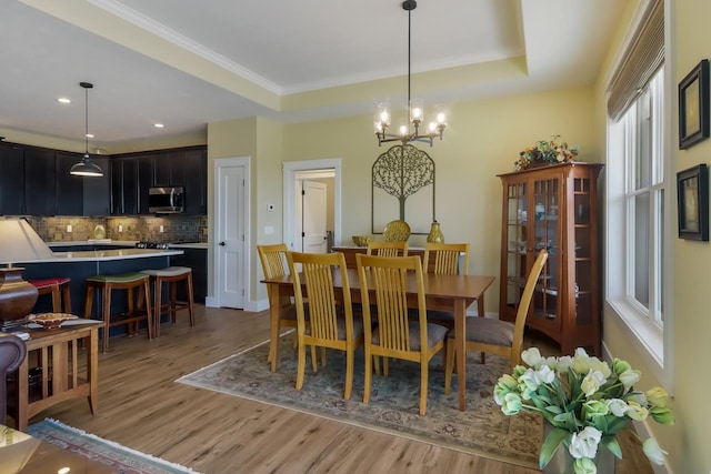 dining space featuring a tray ceiling, a chandelier, crown molding, and light hardwood / wood-style floors