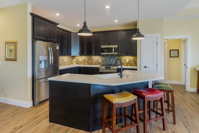 kitchen with a center island with sink, light hardwood / wood-style flooring, hanging light fixtures, and appliances with stainless steel finishes