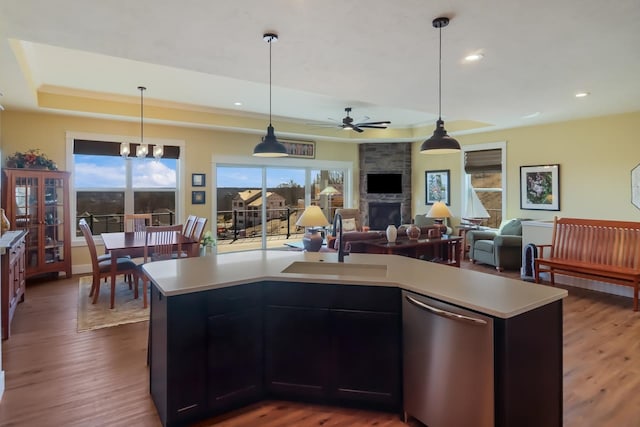 kitchen with sink, dark wood-type flooring, stainless steel dishwasher, a kitchen island with sink, and a fireplace