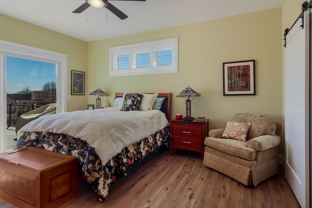 bedroom featuring access to exterior, a barn door, hardwood / wood-style flooring, and ceiling fan