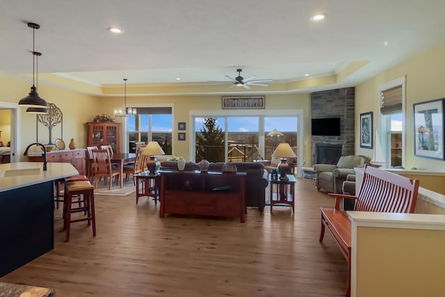 living room with ceiling fan with notable chandelier, dark hardwood / wood-style floors, a stone fireplace, and a healthy amount of sunlight