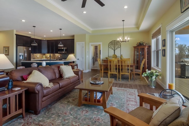 living room featuring sink, ceiling fan with notable chandelier, a raised ceiling, and dark wood-type flooring