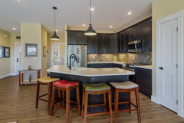 kitchen with dark hardwood / wood-style flooring, pendant lighting, an island with sink, and stainless steel appliances