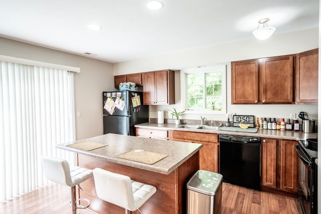 kitchen featuring black appliances, a breakfast bar, light hardwood / wood-style floors, and sink