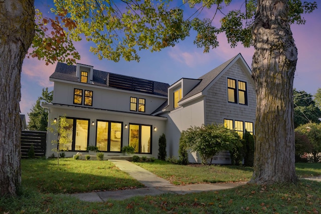 back house at dusk featuring a lawn