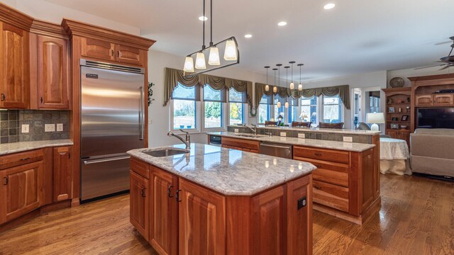 740 Greystone Dr, Chelsea, MI 48118 - kitchen with appliances with stainless steel finishes, an island with sink, a sink, open floor plan, and wood finished floors