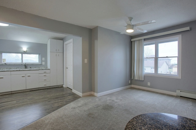 unfurnished living room with a textured ceiling, ceiling fan, a baseboard heating unit, sink, and hardwood / wood-style flooring