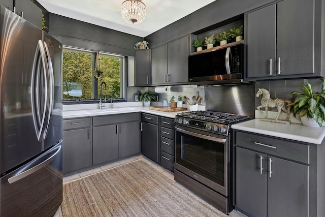 kitchen featuring sink, tasteful backsplash, gray cabinets, light tile patterned flooring, and appliances with stainless steel finishes