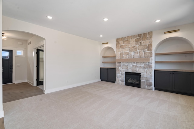 unfurnished living room with a fireplace, built in features, and light carpet