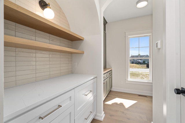 interior space with tasteful backsplash, light stone countertops, white cabinets, and light wood-type flooring