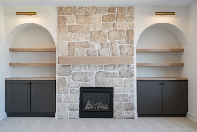 unfurnished living room featuring a stone fireplace, light carpet, and built in features