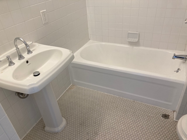 bathroom featuring tile patterned flooring, a bath, tile walls, and toilet