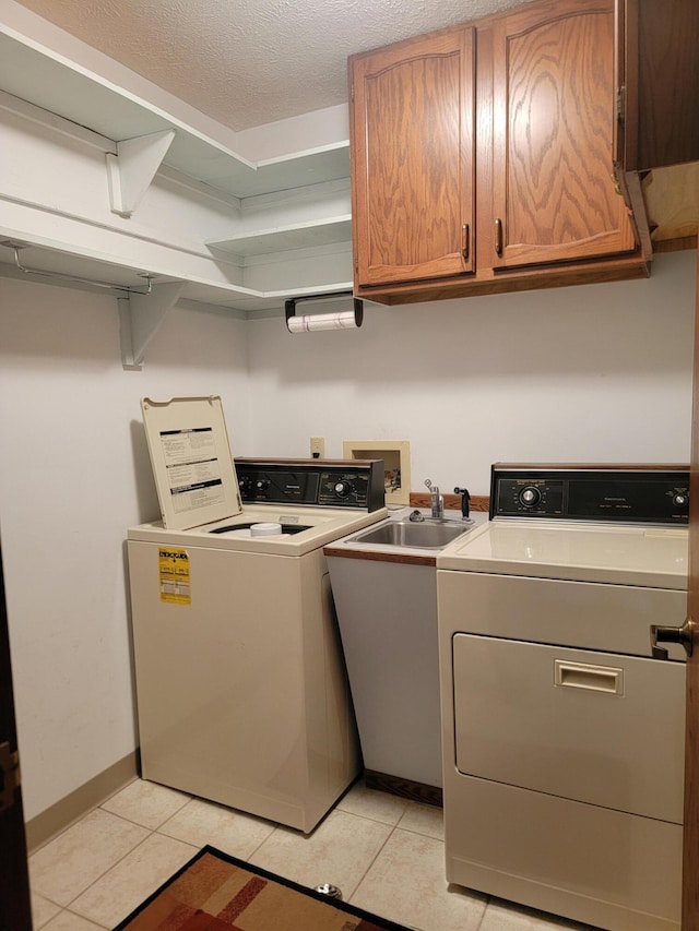 clothes washing area with washing machine and dryer, sink, light tile patterned floors, and cabinets